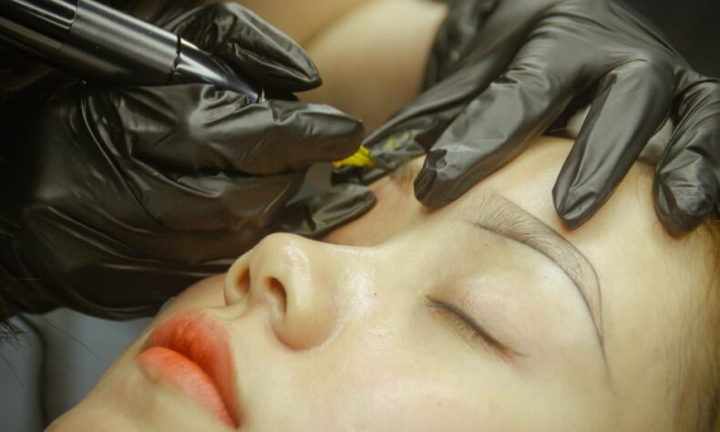 A detailed view of eyebrow microblading procedure with gloved hands and closed eyes. - Photo by Thanh Cong Le on Pexels