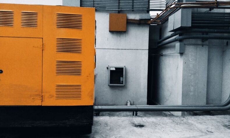 Outdoor view of an industrial generator with visible piping and wiring against a concrete wall. - Photo by ezrah lane on Pexels