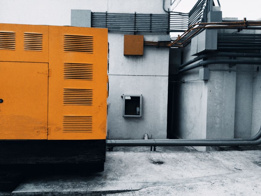 Outdoor view of an industrial generator with visible piping and wiring against a concrete wall. - Photo by ezrah lane on Pexels